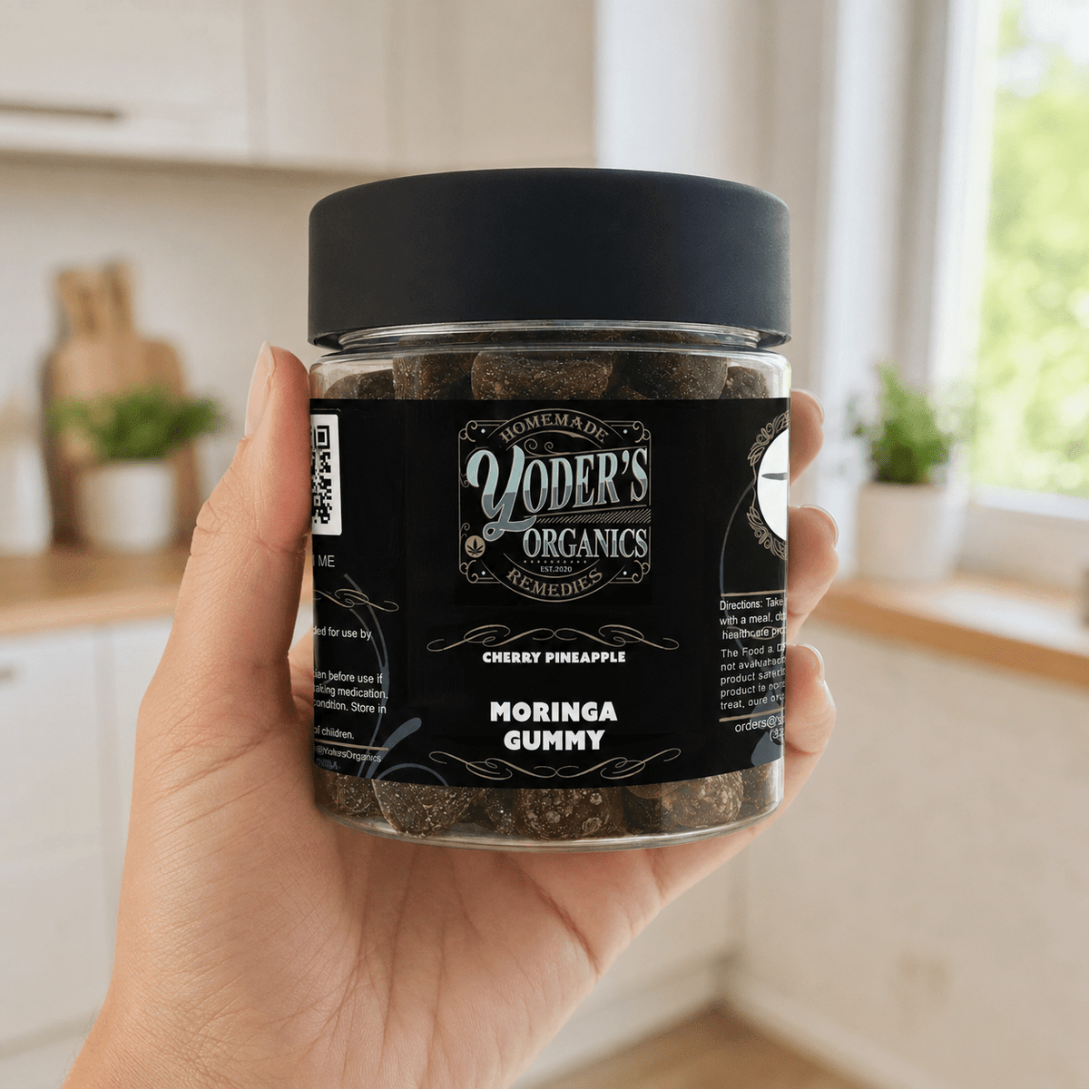 Hand holding a jar of moringa gummies in a kitchen